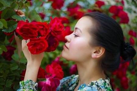 brunette woman smiling in a flowering bush of red roses.の写真素材