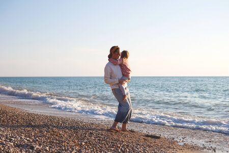 mom and daughter hug and kiss on the beach at sunset.の写真素材