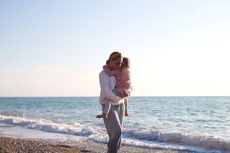 mom and daughter hug and kiss on the beach at sunset.の写真素材