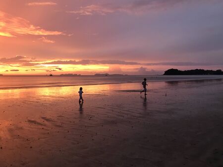 children run on the sand by the ocean at sunset.の写真素材