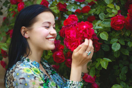 brunette woman smiling in a flowering bush of red roses.の写真素材