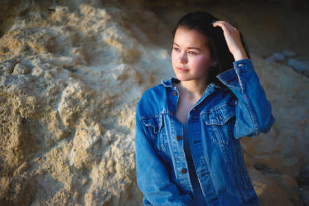 portrait of a woman in a denim jacket on a background of yellow rock.の写真素材