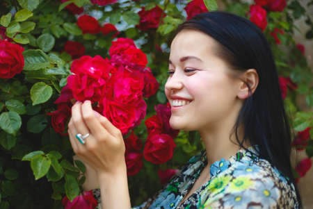 brunette woman smiling in a flowering bush of red roses.の写真素材
