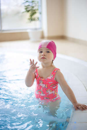 little girl in a pool cap and pink swimsuit learns to swim in the pool.の写真素材