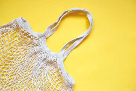 Beige cotton string knitted bag on yellow background. Empty hand made bag. Zero waste, eco friendly...