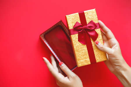 female hands with beautiful manicure open a gift box on a red backgroundの写真素材