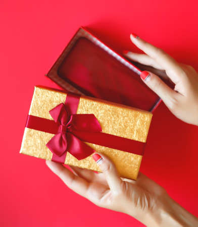 female hands with beautiful manicure open a gift box on a red backgroundの写真素材