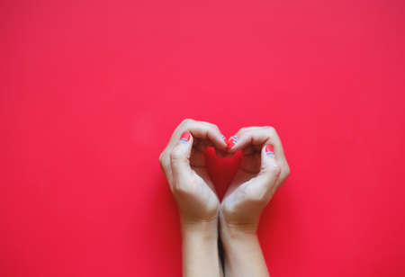 woman's hands with beautiful manicure depict a heart on a red background.の写真素材