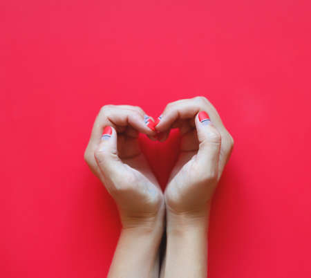 woman's hands with beautiful manicure depict a heart on a red background.の写真素材