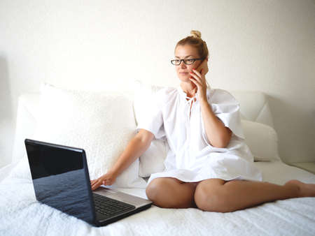 Young woman on a white bed works for a laptop.の写真素材