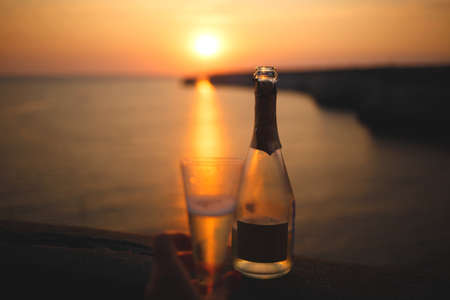 hand with a glass of champagne on the background of the sea and sunset.の写真素材