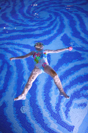 little girl in a pool cap and blue swimsuit learns to swim in the poolの写真素材