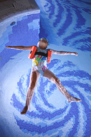 little girl in a pool cap and blue swimsuit learns to swim in the pool.の写真素材