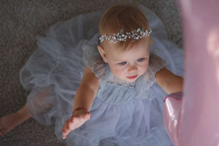 little girl in a beautiful dress pulls her hand to the balloons.
