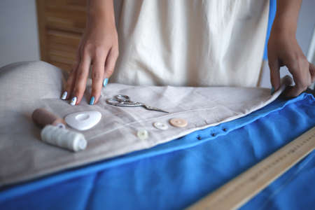hands laying out sewing accessories on a piece of linen fabric on a tailor's table.