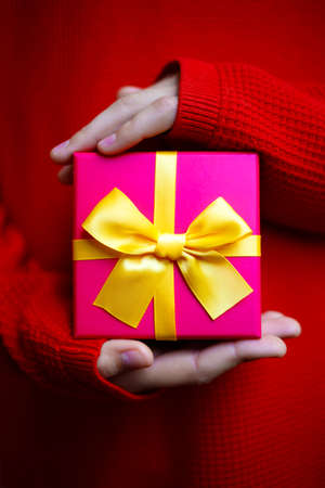 beautiful bright gift in the hands of a child on a red background.の写真素材