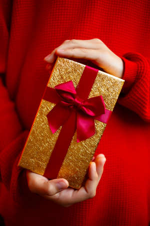 beautiful bright gift in the hands of a child on a red backgroundの写真素材