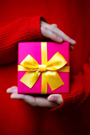 beautiful bright gift in the hands of a child on a red backgroundの写真素材