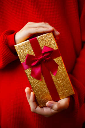 beautiful bright gift in the hands of a child on a red backgroundの写真素材