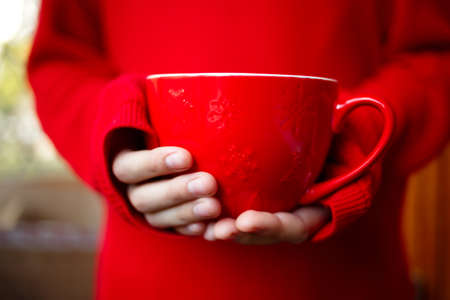 a large mug in the hands of a child on a red backgroundの写真素材