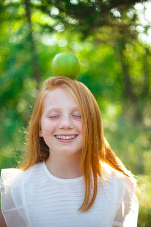 red-haired girl with freckles with an apple on her headの写真素材