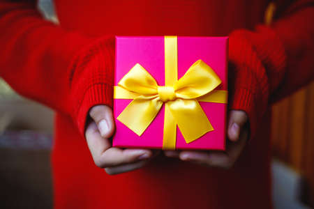 beautiful bright gift in the hands of a child on a red background.の写真素材