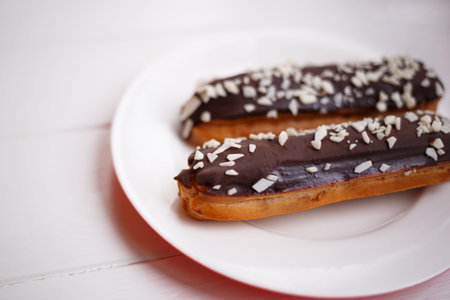 two eclairs on a white plate on a light wooden background