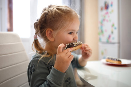 little cute girl eating cake while sitting at the kitchen tableの写真素材