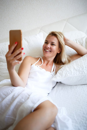 young woman on a white bed is working talking by videoconference.の写真素材