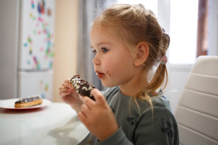 little cute girl eating cake while sitting at the kitchen table.の写真素材