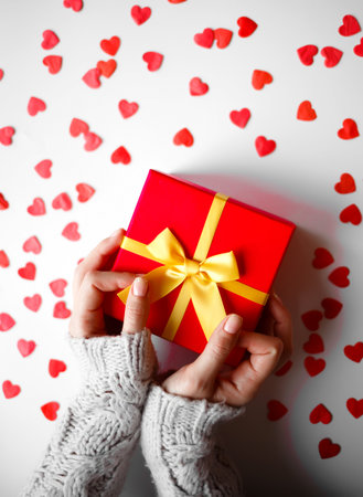 hands hold a gift on a white background with red hearts.の写真素材