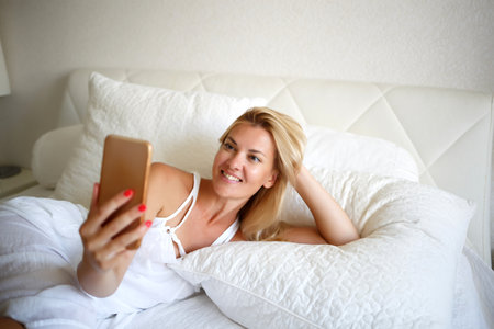 young woman on a white bed is working talking by videoconferenceの写真素材