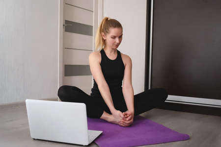 young woman doing asana at home on yoga mat in front of laptop.の写真素材