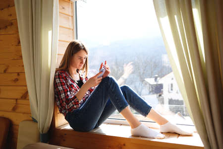 young girl talking on the phone while sitting by the windowの写真素材