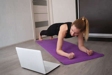 young woman doing asana at home on yoga mat in front of laptopの写真素材