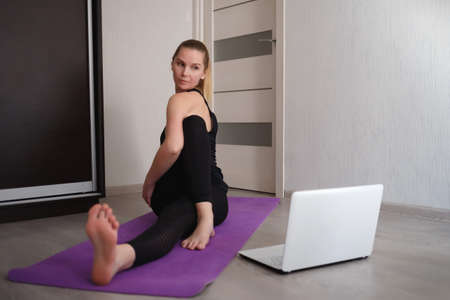 young woman doing asana at home on yoga mat in front of laptopの写真素材