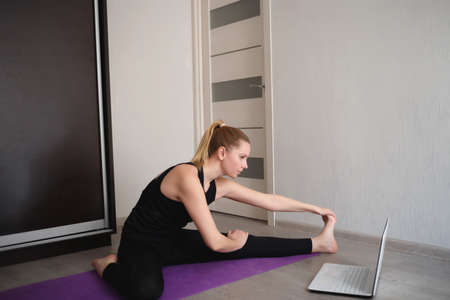young woman doing asana at home on yoga mat in front of laptopの写真素材