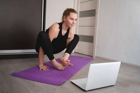 young woman doing asana at home on yoga mat in front of laptopの写真素材