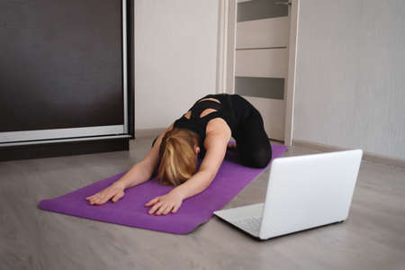young woman doing asana at home on yoga mat in front of laptopの写真素材