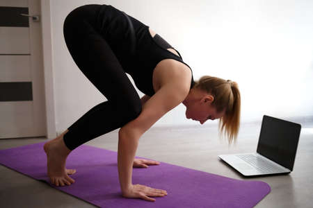 young woman doing asana at home on yoga mat in front of laptopの写真素材