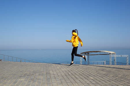 young woman in yellow hoodie jogging by the seaの写真素材
