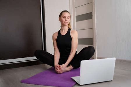 young woman doing asana at home on yoga mat in front of laptop.の写真素材