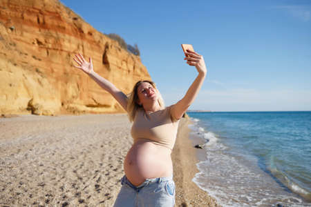 young pregnant woman taking selfie by the sea.