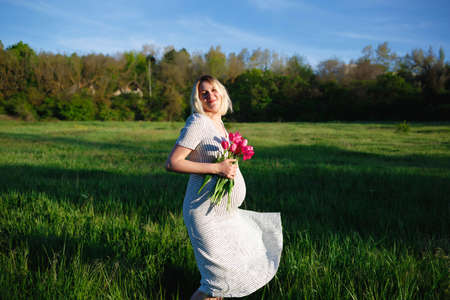 pregnant woman on a green meadow walking with a bouquet of flowersの写真素材