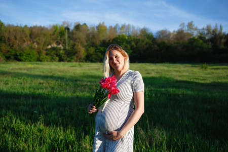 pregnant woman on a green meadow walking with a bouquet of flowersの写真素材