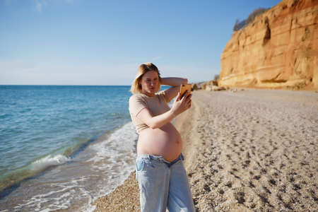 young pregnant woman taking selfie by the seaの写真素材