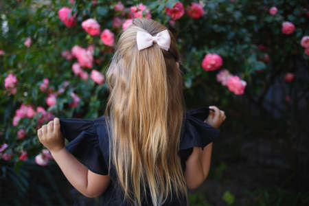 portrait of a little cute girl on the background of bushes of pink roses. back view.の写真素材