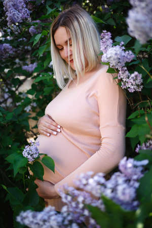 young pregnant woman tenderly hugs her belly surrounded by lilac flowers.の写真素材