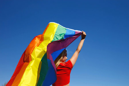 girl with lgbt flag behind her back against a bright blue sky.の写真素材