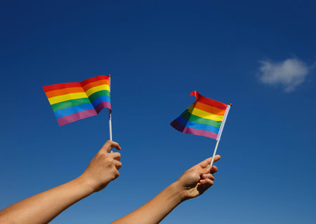 two small lgbt flags in the hands of a couple against the blue sky.の写真素材